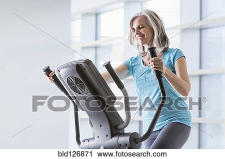 Happy Caucasian woman on elliptical trainer at gym View Large Photo Image Stock Image - Happy Caucasian woman on elliptical trainer at gym. Fotosearch