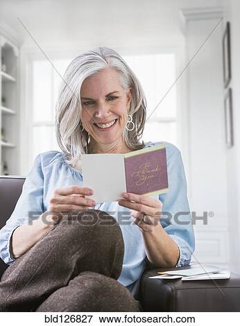 Happy Caucasian woman reading card on sofa View Large Photo Image Stock Photo - Happy Caucasian woman reading card on sofa. Fotosearch