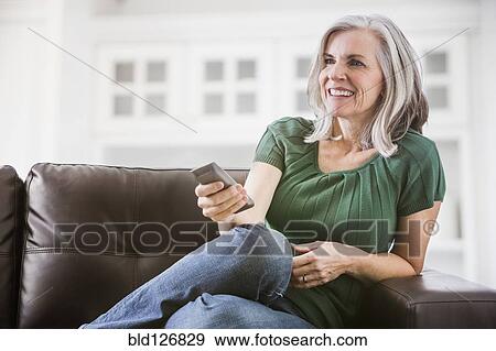 Happy Caucasian woman watching TV on sofa View Large Photo Image Stock Photo - Happy Caucasian woman watching TV on sofa. Fotosearch