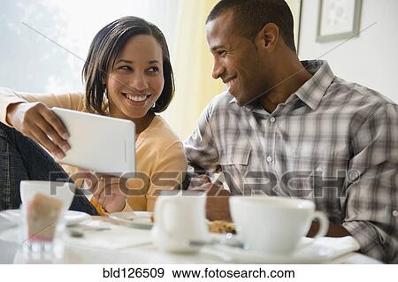 Stock Photo - Happy couple drinking coffee and using digital tablet. Fotosearch