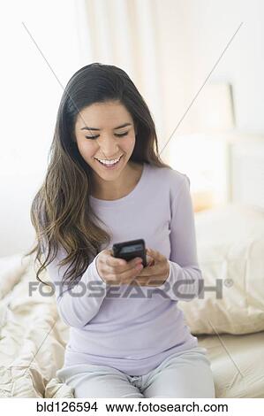 Picture - Happy Hispanic woman text messaging in bed. Fotosearch