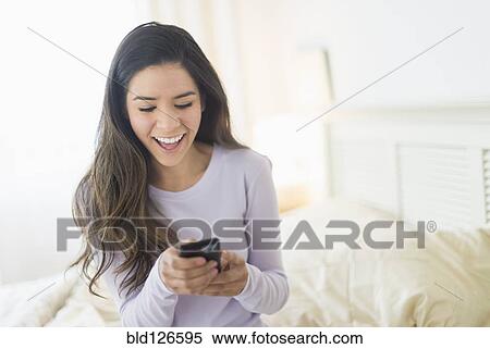 Happy Hispanic woman text messaging in bed View Large Photo Image Stock Photography - Happy Hispanic woman text messaging in bed. Fotosearch