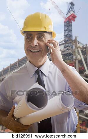 Hispanic architect talking on cell phone at construction site View Large Photo Image Stock Image - Hispanic architect talking on cell phone at construction site. Fotosearch