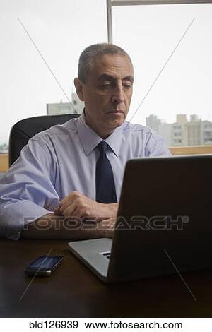 Stock Photo - Hispanic businessman using laptop in office. Fotosearch