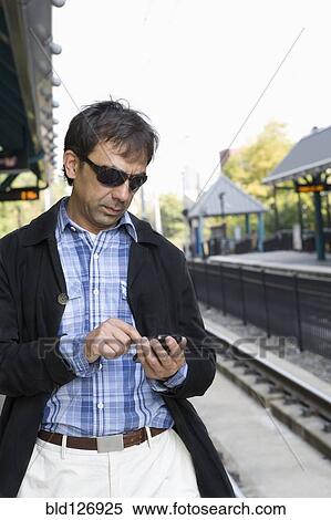 Stock Photography - Hispanic man text messaging on train station platform. Fotosearch