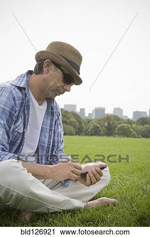 Hispanic man using cell phone in grass at park View Large Photo Image Stock Image - Hispanic man using cell phone in grass at park. Fotosearch