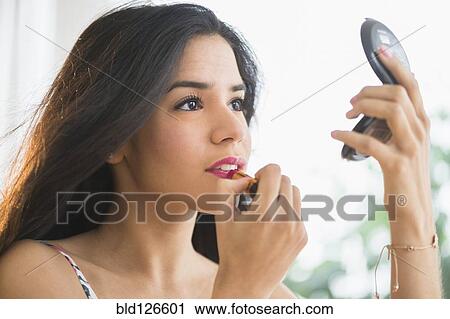 Stock Image - Hispanic woman applying lipstick in compact mirror. Fotosearch