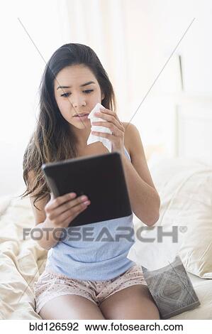 Stock Image - Hispanic woman holding tissue and using digital tablet in bed. Fotosearch