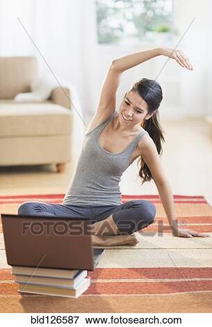 Stock Photo - Hispanic woman on rug stretching in front of laptop. Fotosearch