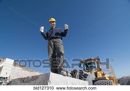 Stock Image - joyful worker on top of marble slab in quarry. Fotosearch