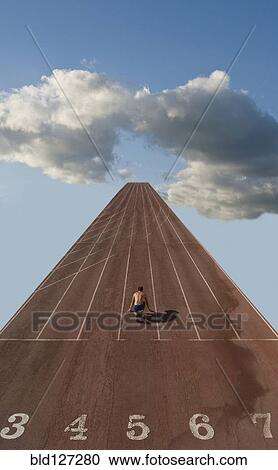 Stock Image - Lone sprinter at starting position on track in clouds (Digital Composite). Fotosearch