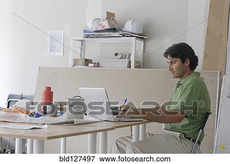 Male architect using laptop on makeshift desk in site office View Large Photo Image Stock Photo - Male architect using laptop on makeshift desk in site office. Fotosearch