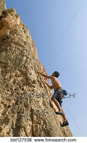 Stock Photo - Male free climber scaling rock face low angle view. Fotosearch