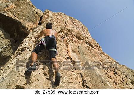 Male free climber scaling rock face rear view low angle view View Large Photo Image Stock Photo - Male free climber scaling rock face rear view low angle view. Fotosearch