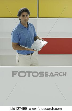 Stock Photo - Male office worker holding book in front of coloured shelves portrait. Fotosearch
