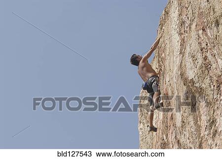 Male rock climber scaling rock face secured by ropes low angle view View Large Photo Image Stock Image - Male rock climber scaling rock face secured by ropes low angle view. Fotosearch