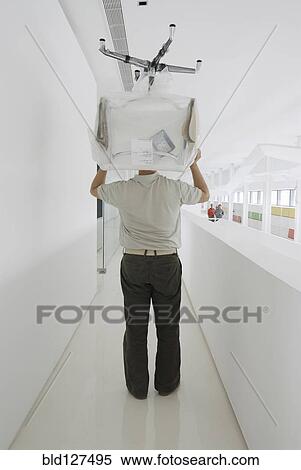 Stock Photography - Man carrying chair thorugh office rear view. Fotosearch