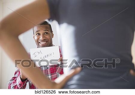 Stock Photograph - Man showing 'I'm Sorry' sign to angry girlfriend. Fotosearch