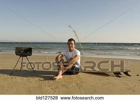 man sitting on beach with surfboard and barbecue View Large Photo Image Stock Photo - man sitting on beach with surfboard and barbecue. Fotosearch