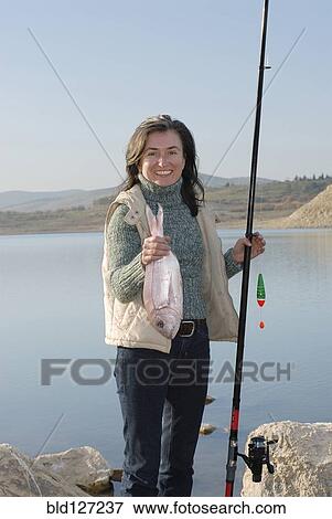 Mature woman at lakeside holding fishing rod and fish smiling portrait View Large Photo Image Stock Photo - Mature woman at lakeside holding fishing rod and fish smiling portrait. Fotosearch