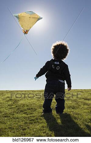 Stock Photo - Mixed race boy watching kite flying against blue sky. Fotosearch