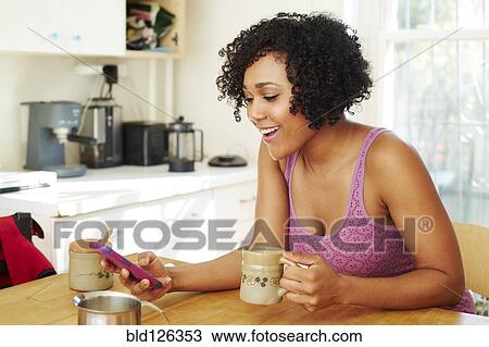 Mixed race woman using cell phone and drinking coffee in kitchen View Large Photo Image Stock Image - Mixed race woman using cell phone and drinking coffee in kitchen. Fotosearch