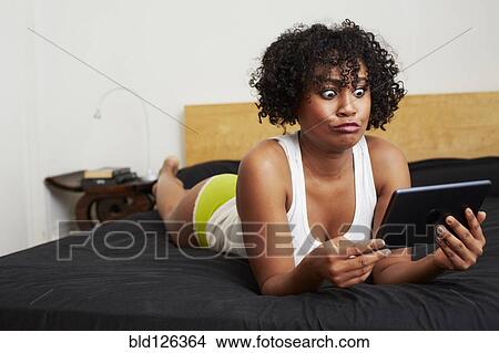 Mixed race woman using digital tablet on bed View Large Photo Image Picture - Mixed race woman using digital tablet on bed. Fotosearch