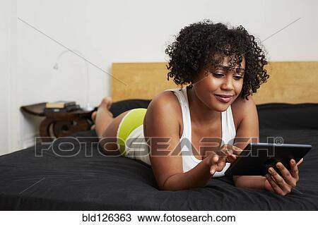 Mixed race woman using digital tablet on bed View Large Photo Image Stock Image - Mixed race woman using digital tablet on bed. Fotosearch
