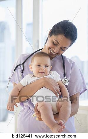 Stock Image - Nurse holding smiling baby. Fotosearch