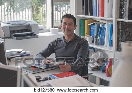 Stock Image - office worker sitting at desk smiling to camera. Fotosearch