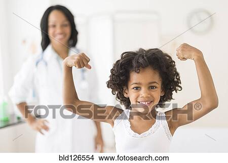 Portrait of African American girl flexing muscles in doctor's office View Large Photo Image Picture - Portrait of African American girl flexing muscles in doctor's office. Fotosearch