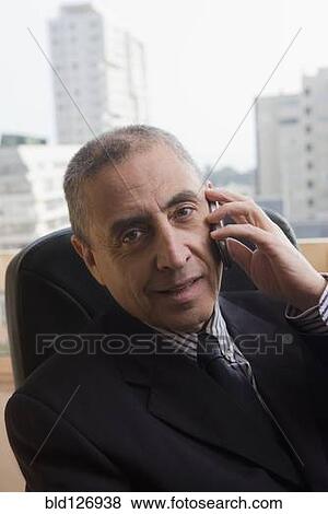 Stock Photo - Portrait of Hispanic businessman talking on cell phone in office. Fotosearch