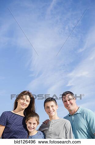 Stock Photograph - Portrait of smiling Caucasian family under blue sky. Fotosearch