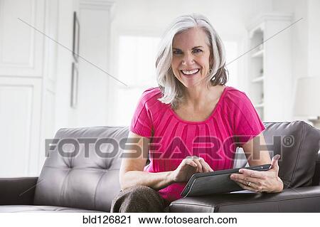 Stock Image - Portrait of smiling Caucasian woman using digital tablet on sofa. Fotosearch