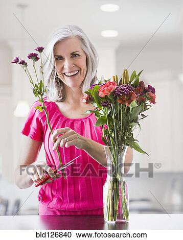 Stock Image - Portrait of smiling Caucasian woman arranging flowers. Fotosearch