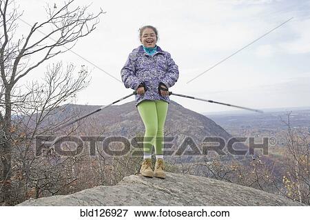 Stock Photo - Portrait of smiling Hispanic girl on rock with hiking poles. Fotosearch