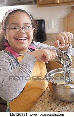 Stock Image - Portrait of smiling Hispanic girl baking in kitchen. Fotosearch