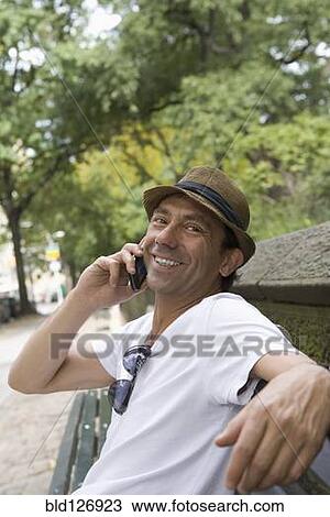 Stock Image - Portrait of smiling Hispanic man talking on cell phone in park. Fotosearch