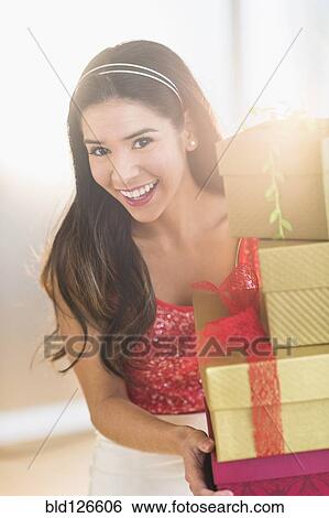 Stock Photograph - Portrait of smiling Hispanic woman carrying Christmas gifts. Fotosearch