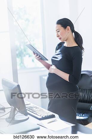 Stock Image - Pregnant Japanese businesswoman using digital tablet. Fotosearch