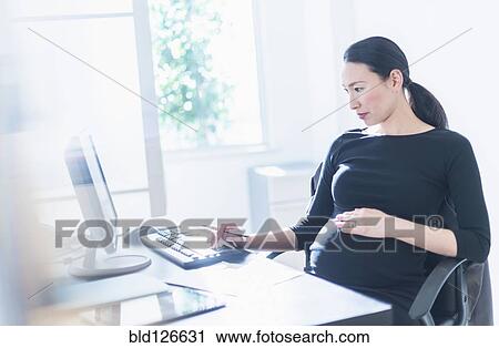 Stock Image - Pregnant Japanese businesswoman using computer. Fotosearch