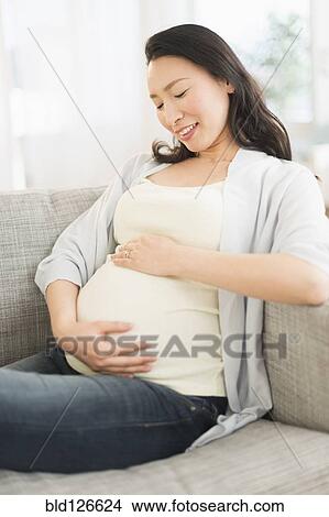 Picture - Pregnant Japanese woman holding stomach. Fotosearch