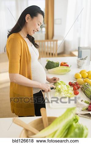 Pregnant Japanese woman slicing vegetables in kitchen View Large Photo Image Stock Photo - Pregnant Japanese woman slicing vegetables in kitchen. Fotosearch