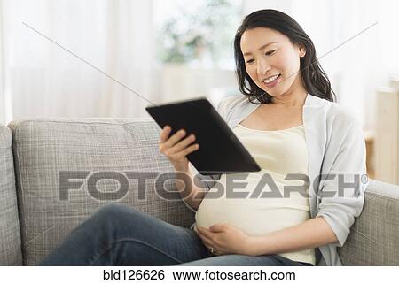 Pregnant Japanese woman using digital tablet on sofa View Large Photo Image Stock Photograph - Pregnant Japanese woman using digital tablet on sofa. Fotosearch