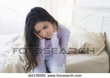 Stock Image - Sad Hispanic woman sitting at edge of bed. Fotosearch