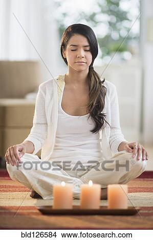 Picture - Serene Hispanic woman meditating near lit candles. Fotosearch
