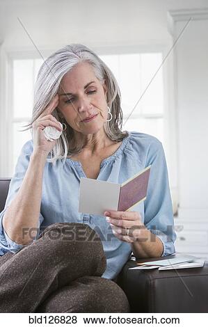Serious Caucasian woman reading card on sofa View Large Photo Image Stock Photo - Serious Caucasian woman reading card on sofa. Fotosearch