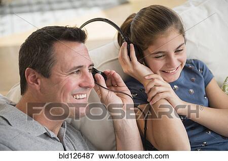 Stock Photo - Smiling Caucasian father and daughter sharing headphones. Fotosearch