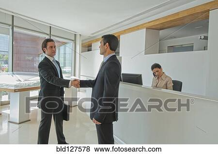 Stock Photo - two businessmen shaking hands in office reception. Fotosearch