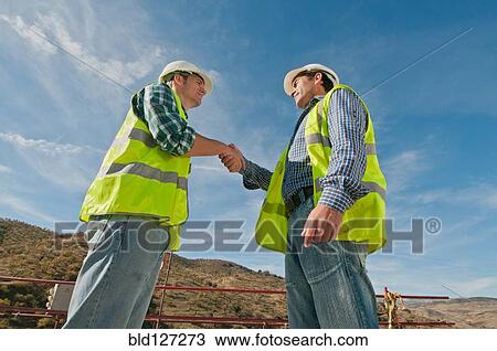 Stock Image - Two construction engineers shaking hands. Fotosearch